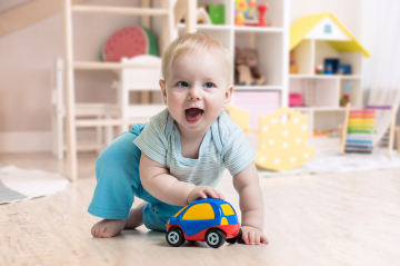 Ein kleiner Junge spielt am Boden mit einem Spielzeugauto.