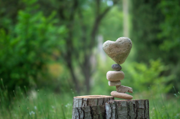 Ein Holzstumpf im Wald mit Steinen die aufeinander balancieren mit einem Herzstein als Abschluss