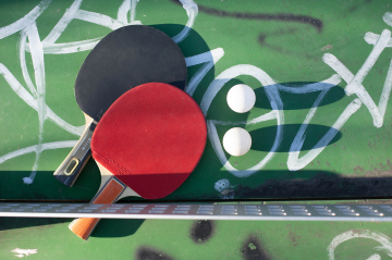 Zwei Tischtennisschläger und Bälle auf einer Tischtennisplatte die mit Graffiti bemalt ist