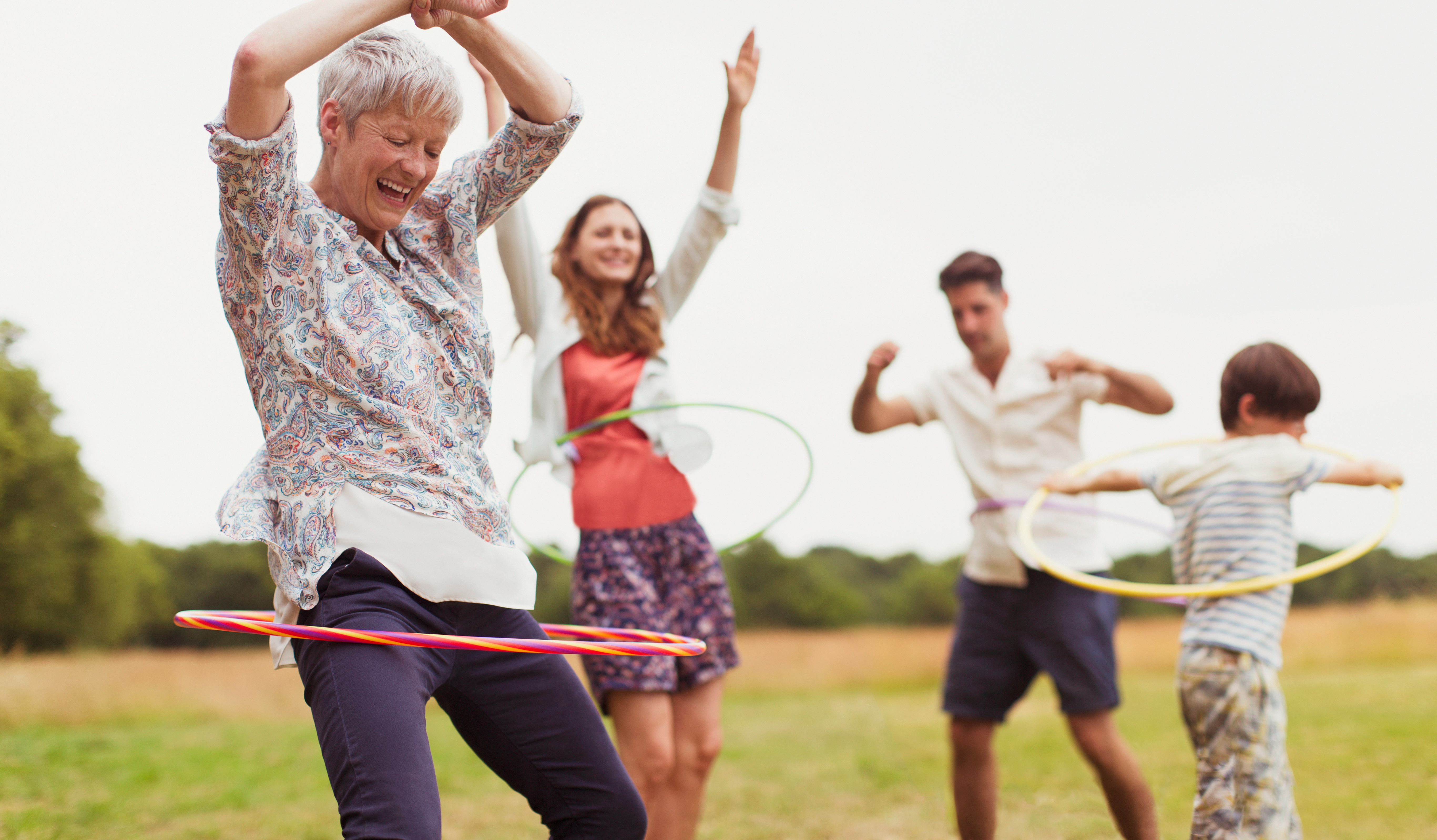 Eine Familie spielt auf einer Wiese am Waldrand Hoola-Hoop.