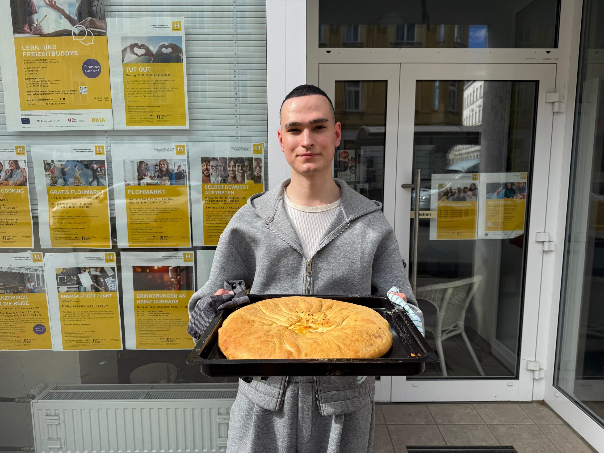 John präsentiert selbstgebackenen ossetischen Kuchen vor dem Sprachencafé