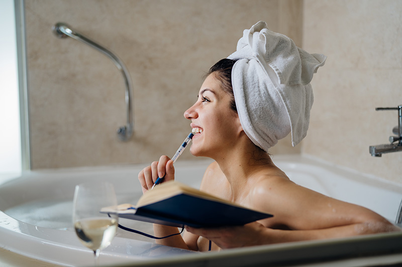 Eine junge Frau sitzt mit einem Notizbuch in der Badewanne und macht sich Gedanken