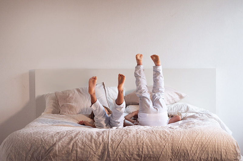 Zwei Kinder liegen im Bett und strecken ihre Füße in die Höhe
