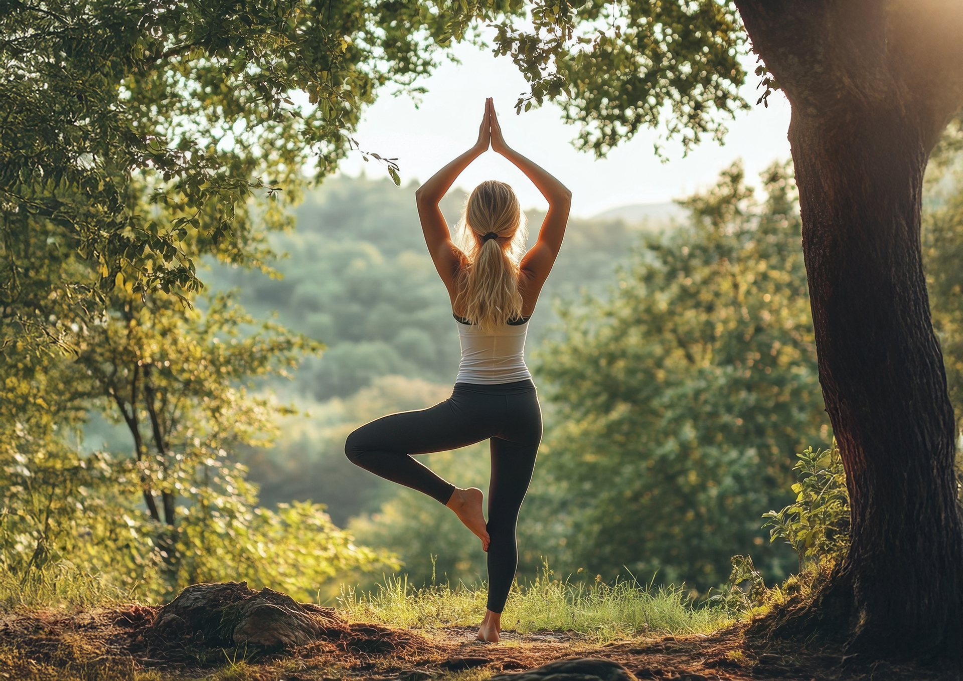 Junge Frau steht in einbeiniger Yoga-Position im Wald.