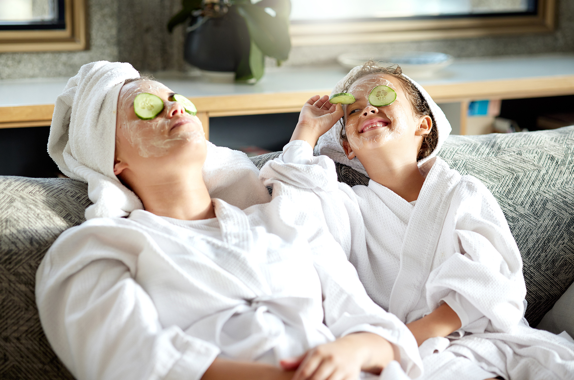 Mutter und Kind liegen in Bademantel auf der Couch und entspannen sich mit einer Gesichtsmaske.