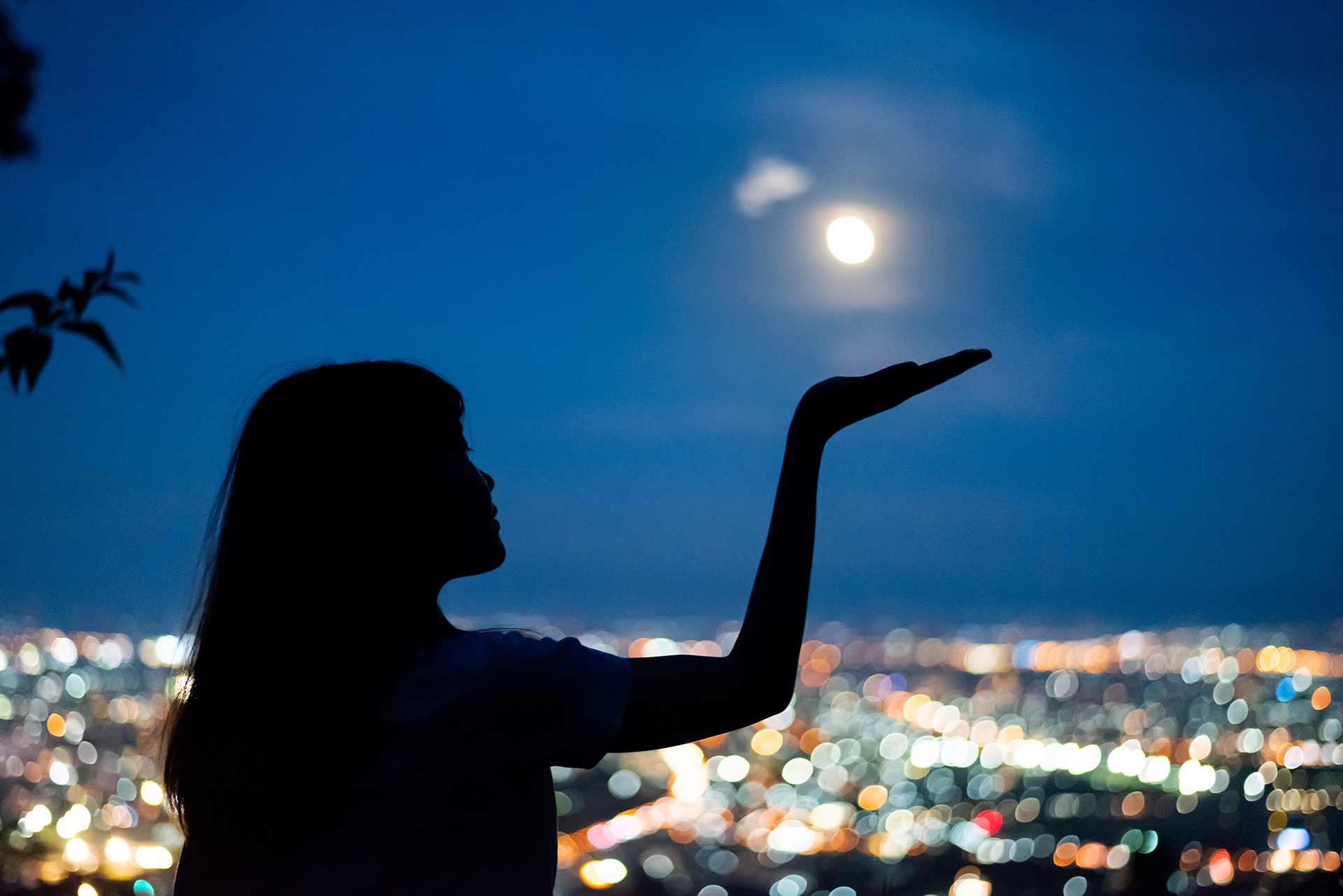 Junge Frau hält Hand in den Nachthimmel, als würde sie den Mond tragen.