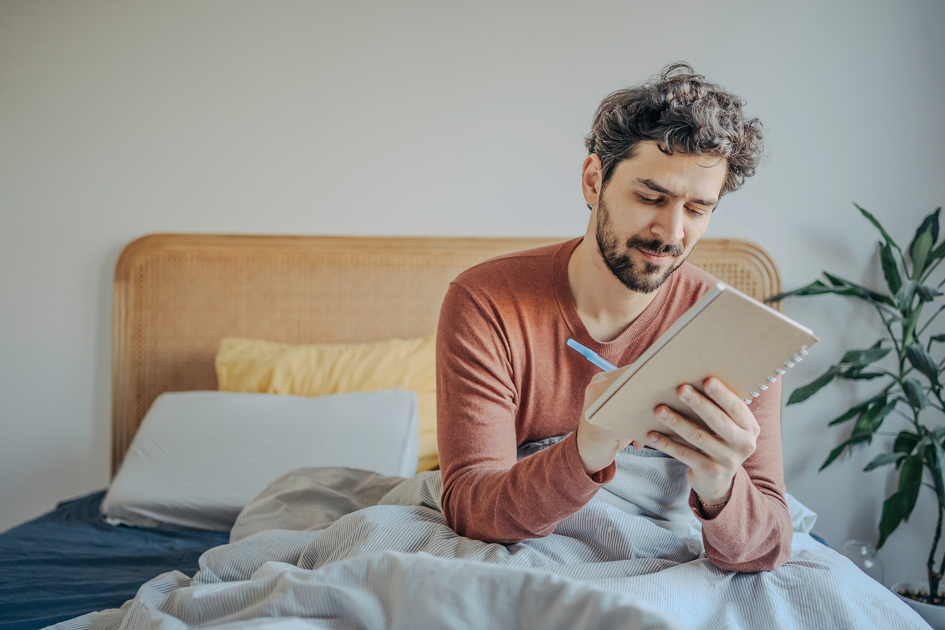 Ein Mann sitzt im Bett und schreibt eine Liste. 