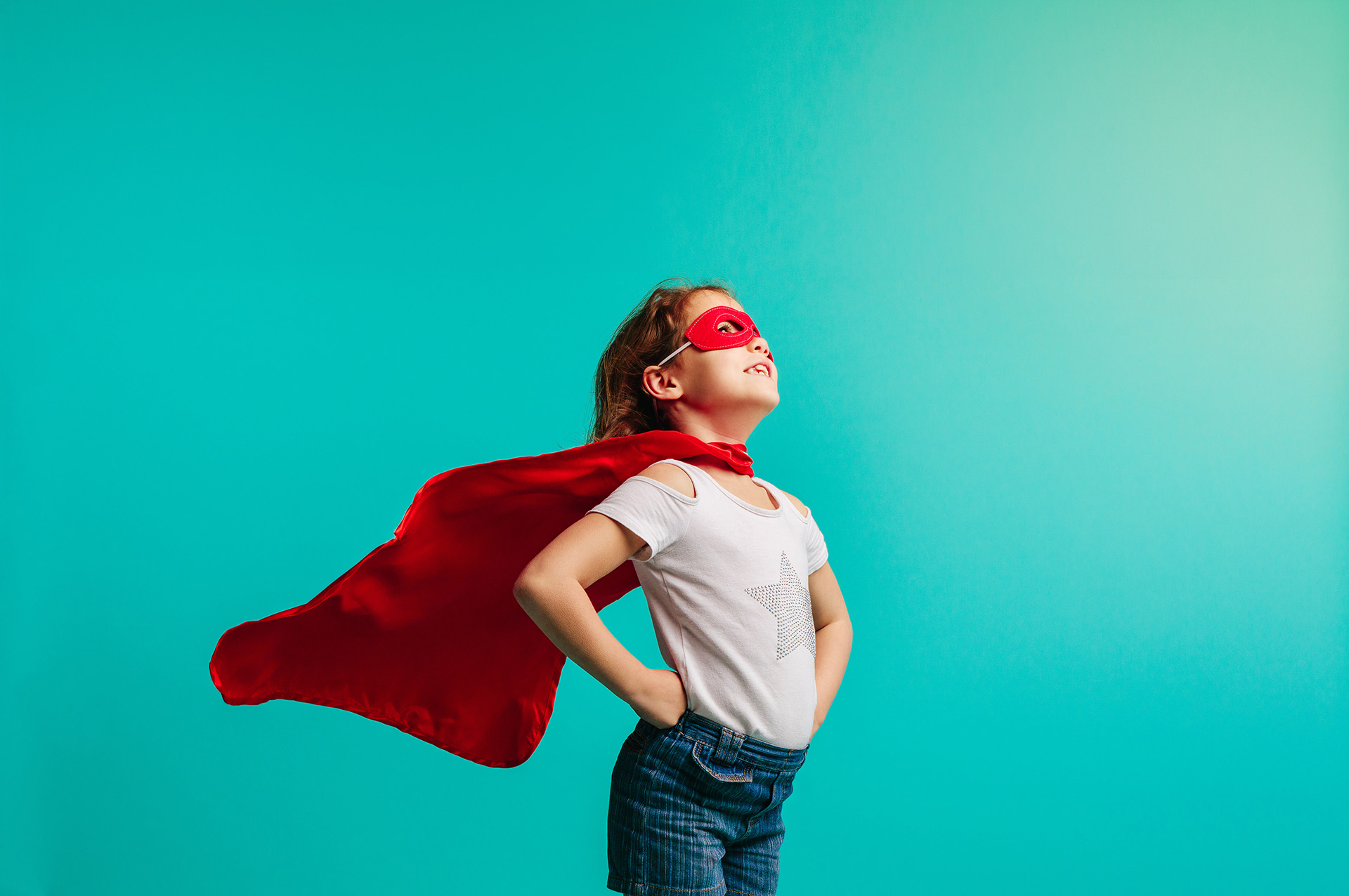 Ein verkleidetes Mädchen steht stolz mit ihrer Heldinnenmaske und Umhang.