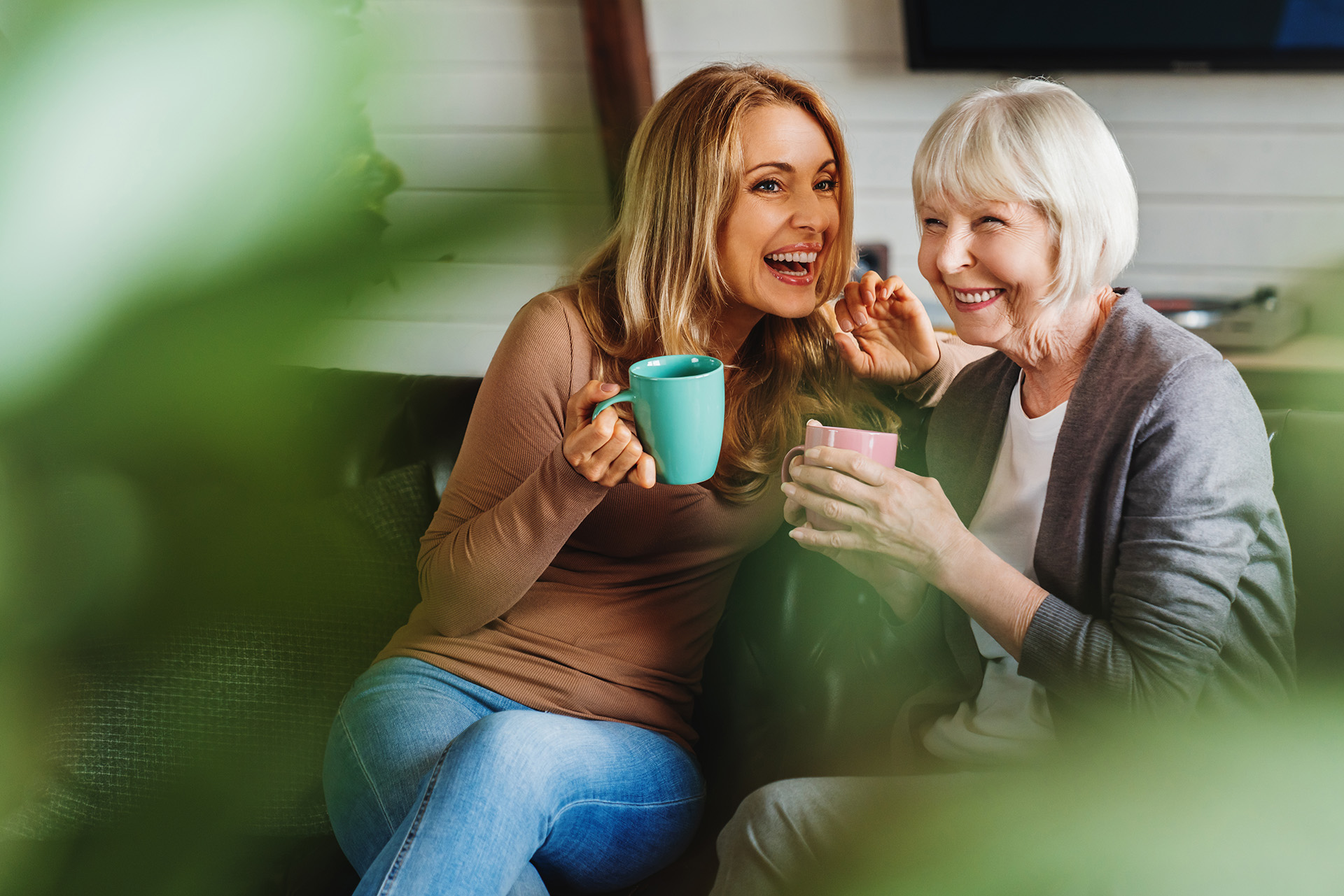 Eine junge und eine ältere Frau unterhalten sich auf der Couch bei einer Tasse Kaffee.