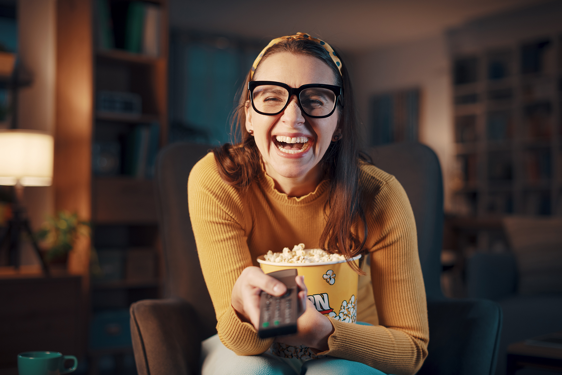 Eine Frau mit einer Popcorntüte in der Hand lacht zu einem lustigen Film.
