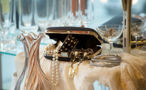 In einer Schatulle liegen stilvoller Schmuck, umgeben von gut erhaltenen Vasen und Gläsern.