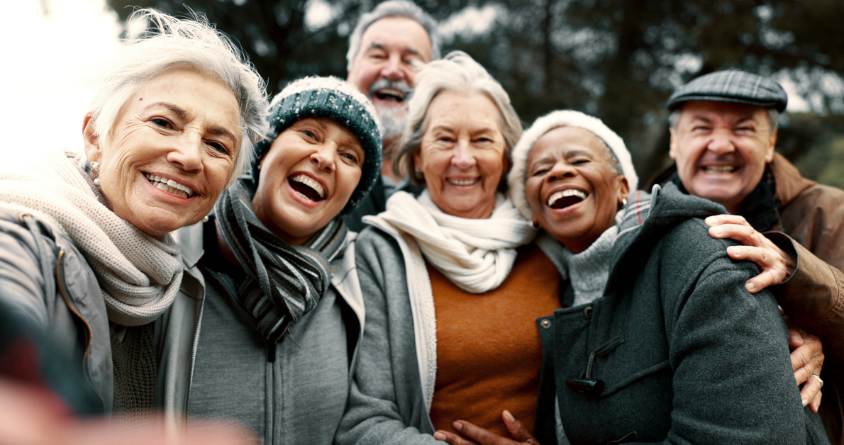 6 erwachsene Frauen und Männer in warmer Kleidung machen ein stimmungsvolles Selfie.