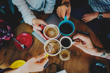 Hände stoßen einander mit vollen Kaffeetassen an