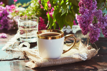 Schön dekorierter Tisch mit Blumen, Kaffeetasse mit Goldrand und einem Glas Wasser