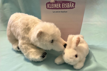 Zwei Kuscheltiere in weiß - ein Eisbär und ein Hase dahinter das Bilderbuch Kleiner Eisbär stehend
