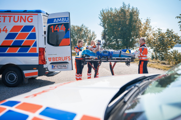 Rettungssanitäter stehen um eine fahrbare Rettungstrage vor den geöffneten Hecktüren eines Rettungswagen