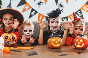 Kinder mit bunt gemalten Gesichtern feiern Halloween mit leuchtenden Kürbissen 