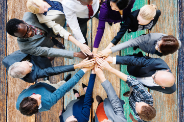 Eine Gruppe Menschen steht im Kreis und hat die Hände übereinander gelegt.