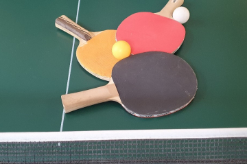 Tischtennis-Tisch auf dem 3 Tischtennis-Schläger und ein Ball liegen.