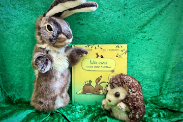 Zwei Kuscheltiere - ein Hase und ein Igel, dahinter das Bilderbuch 